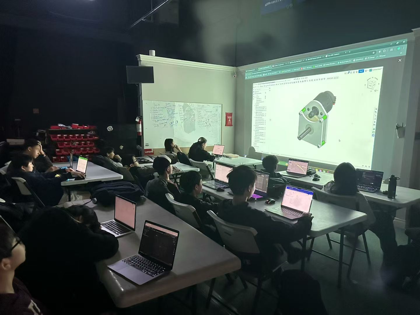 Students participating in a hands-on workshop with laptops and a projected 3D design.